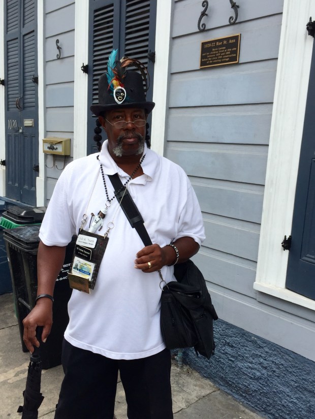 NU'Awlons Natescott stands in front of where Marie Laveau's house once stood. The plaque reads, "1020-22 Rue St. Ann - Marie Laveau and her children lived at this site between 1839 and 1895 before the circa 1905 construction of the existing cottage.